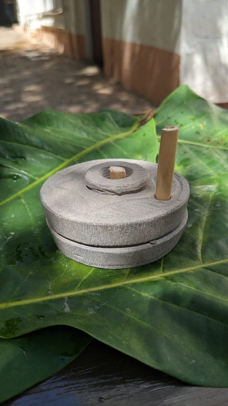 Traditional stone jaata used at Madhuved to grind pulses, resting on a green leaf