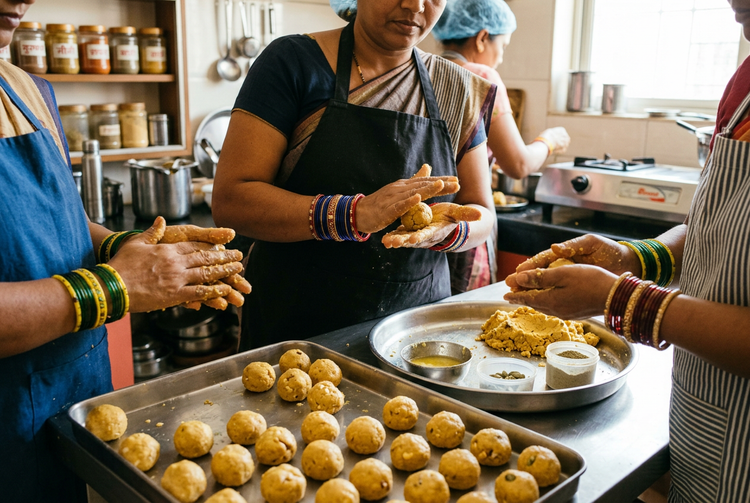 Women shaping besan ladoos by hand on steel trays